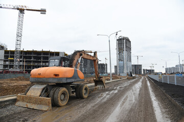 Bucket wheel excavator on road work at construction site. Backhoe digs digs the ground to lay pipes and a new road. Tower cranes are building tall residential buildings.