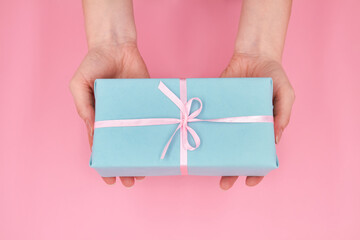 A woman holding in hands Christmas or New Year gift box against a pink background