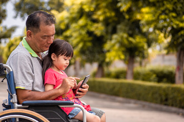 Fototapeta premium Grandfather and granddaughter Play the smart phone on the wheelchair.