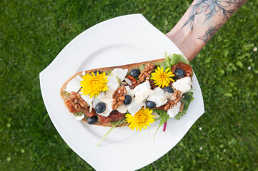 Hand holding a white plate with bread decorated with cheese, blueberries and flowers