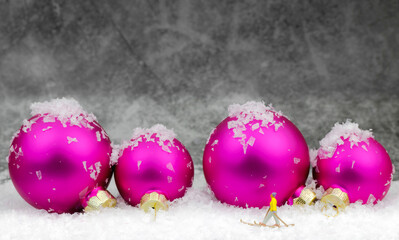 miniature skier in front of pink christmas balls on grey background 