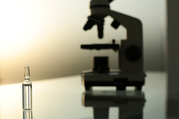 Ampoule with a vaccine and a microscope on a glass table