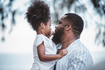 African American father carrying his daughter and kisses on the cheek with cheerful loving. Happy family.