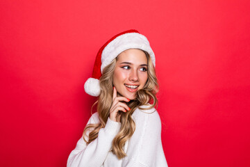 Young pretty woman in warm clothes in santa hat isolated on red background