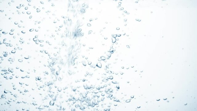 Water stream in slow motion falls on smooth clean surface, creating air bubbles, drop splashes after falling. Freshness of a clear blue liquid poured into transparent container on white background