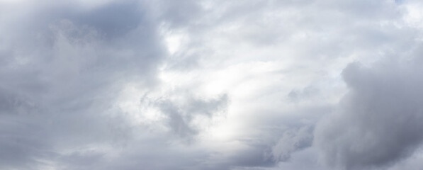 Cloudy sky with gray clouds and a light gap in the center, panorama of the sky