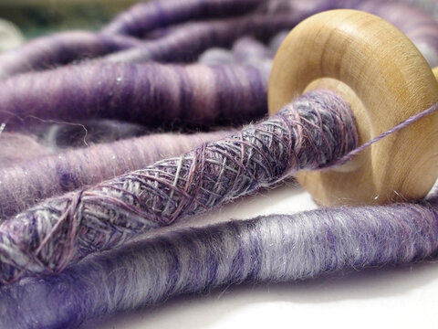 spinning yarn on spindle with rolls (rolags) of purple silk and wool blend fibers