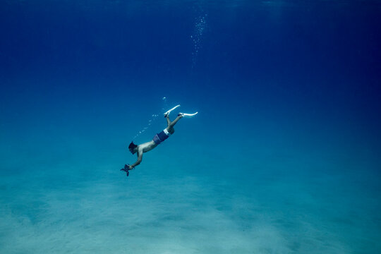 Underwater photographer free diving deep to ocean floor in hawaii