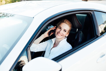 Beautiful fashionable woman blonde talking on the phone behind the wheel of a white car