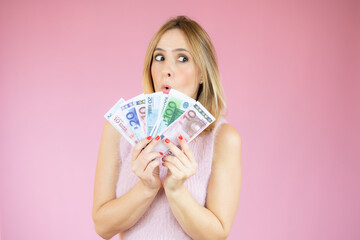 Image of young funny woman standing over pink wall wearing casual clothes holding money. Looking aside.
