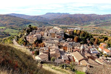 High angel view of beautiful small old town on the hill surrounded by mountains and colorful autumn trees against nice blue and clouds sky during autumn in Pennabilli,Province of Rimini,Italy