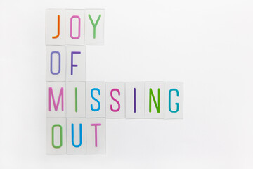 Abbreviation word JOMO, multicolored plastic letters on white background. JOMO - Joy Of Missing Out. Opposition, choice, social problem, digital detox. Flat lay, copy space, minimalism style