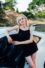 Obraz na płótnie Canvas Beautiful female blonde in black dress stands by white sports car