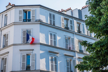 View of the building and the flag of France in the window on a clear sunny day in Paris