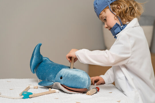 young child wearing medical PPE examines a plush toy whale by taking its temperature with a thermometer