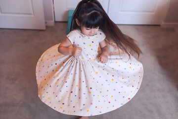 Preschool twirling in her bedroom, wearing a polka dot dress.