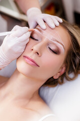 make up and beauty concept - close up portrait of cosmetologist drawing perfect shape of eyebrows