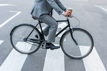 Fototapeta premium Cropped view of businessman holding takeaway coffee while cycling on crosswalk