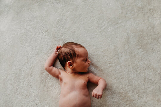 Newborn baby arms, belly and head laying on a white blanket