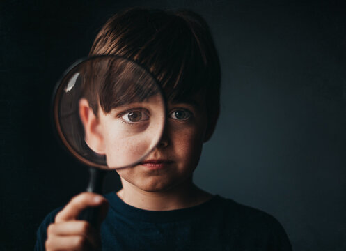 Portrait of young boy holding a magnifying glass over one eye.