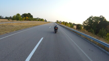 Follow to biker riding on modern sport motorbike at highway during sunny autumn day. Motorcyclist racing his motorcycle on country road. Guy drive bike during trip. Concept of journey. Aerial shot