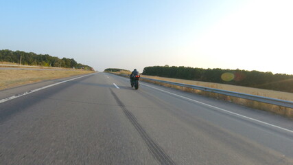 Fototapeta premium Follow to biker riding on modern sport motorbike at autumn highway. Motorcyclist racing his motorcycle on country road. Man driving bike during trip. Concept of freedom and adventure. Aerial shot