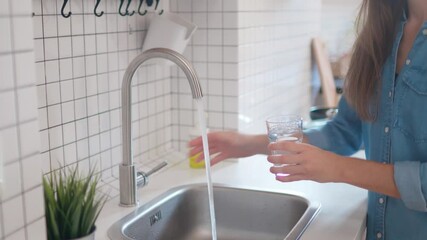 Woman pouring clean filtered water from the tap in glass for drinking at modern loft style kitchen