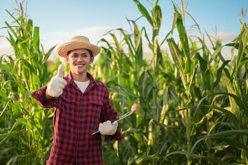 Young farmer in a corn field smiles at the camera while raising his hand to express joy.