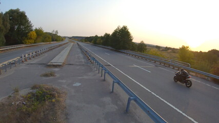 Fototapeta premium Follow to biker riding on modern sport motorbike on country road at sunset. Motorcyclist racing his motorcycle at highway. Guy driving bike during trip. Concept of journey and freedom. Aerial shot