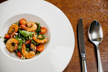 Fresh salad plate with shrimp, tomato and mixed greens on wooden background close up. Healthy food. Clean eating.