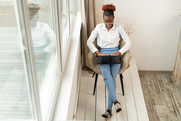 beautiful young african female sitting with a laptop indoors near the window