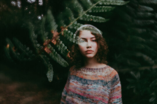 Girl standing behind leaves in sweater and hat