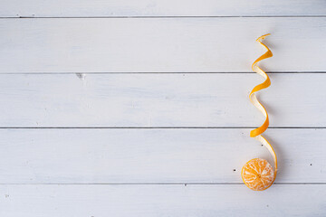 Mandarine mit geschälter Schale als Spirale geformt, auf weißem Holzuntergrund, rechts von unten...