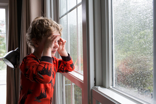 Young Boy Looks Through Rain Covered Window With Pretend Binoculars