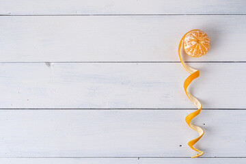 Mandarine mit geschälter Schale als Spirale geformt, auf weißem Holzuntergrund, rechts von oben...