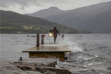 A person carrying a lantern at the edge of a dock in Norway