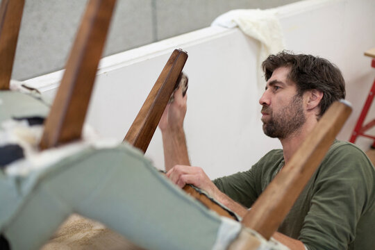 A focused craftsman polishes the leg of an antique chair