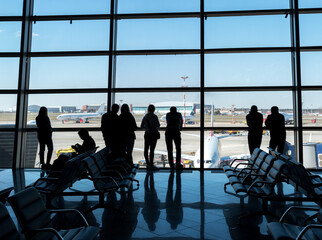 Silhouettes of passengers at the airport Vnukovo in the waiting hall against the background of the airfield and aircraft.