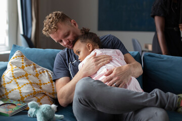 A father holding his young daughter on the couch