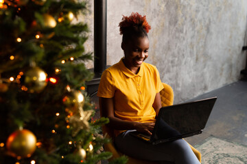beautiful young african female sitting with laptop indoors near christmas tree