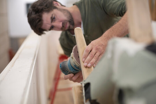 A focused man sands the leg of a chair