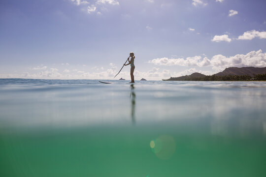 Young girl paddleboards in turquoise water on a clear morning.
