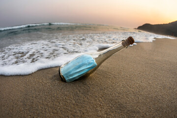 Surgical face mask inside a glass bottle at the beach