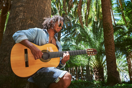 Young musician with classical guitar playing under the shade of some trees in a park.