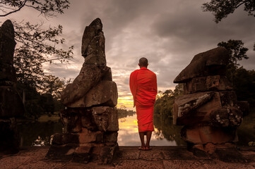 SIEM REAP, CAMBODIA - 15 SEPTEMBER 2012: Monk stands among ancient statues of south gate of Angkor Thom at sunset.