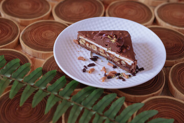 chocolate dessert in a cut with filling of caramel, nuts and nougats. The cake is covered with chocolate on a wooded background with a morning natural light