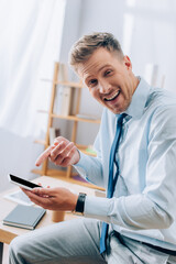 Cheerful businessman pointing at smartphone with blank screen in office