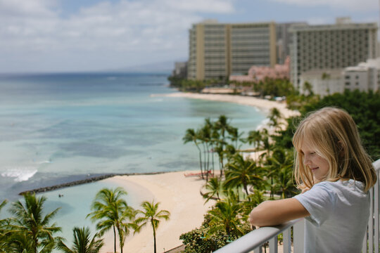 Smiling girl enjoys Waikiki ocean view from hotel balcony (tilt shift)