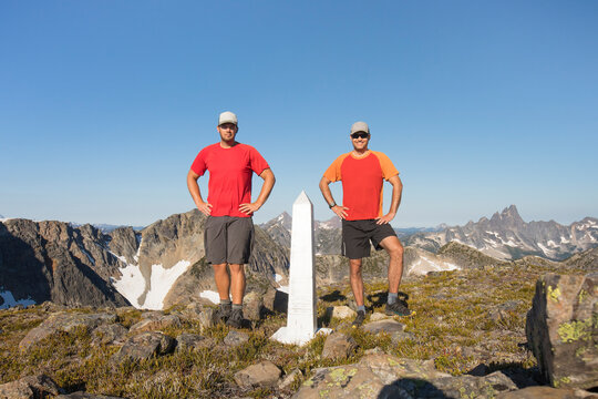 Two trail runners stand at the border marker, Canada / United State