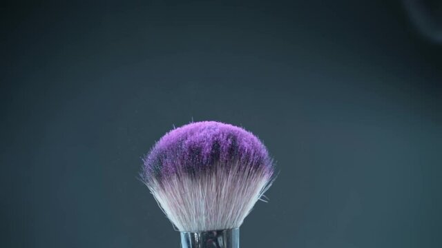 Cosmetic brushes with purple eyeshadow splashing on black